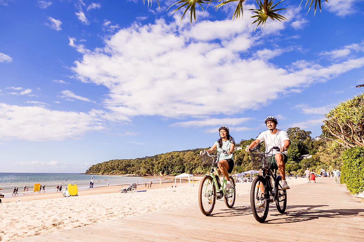 Couple riding e-Bikes along the beachfront path in Noosa