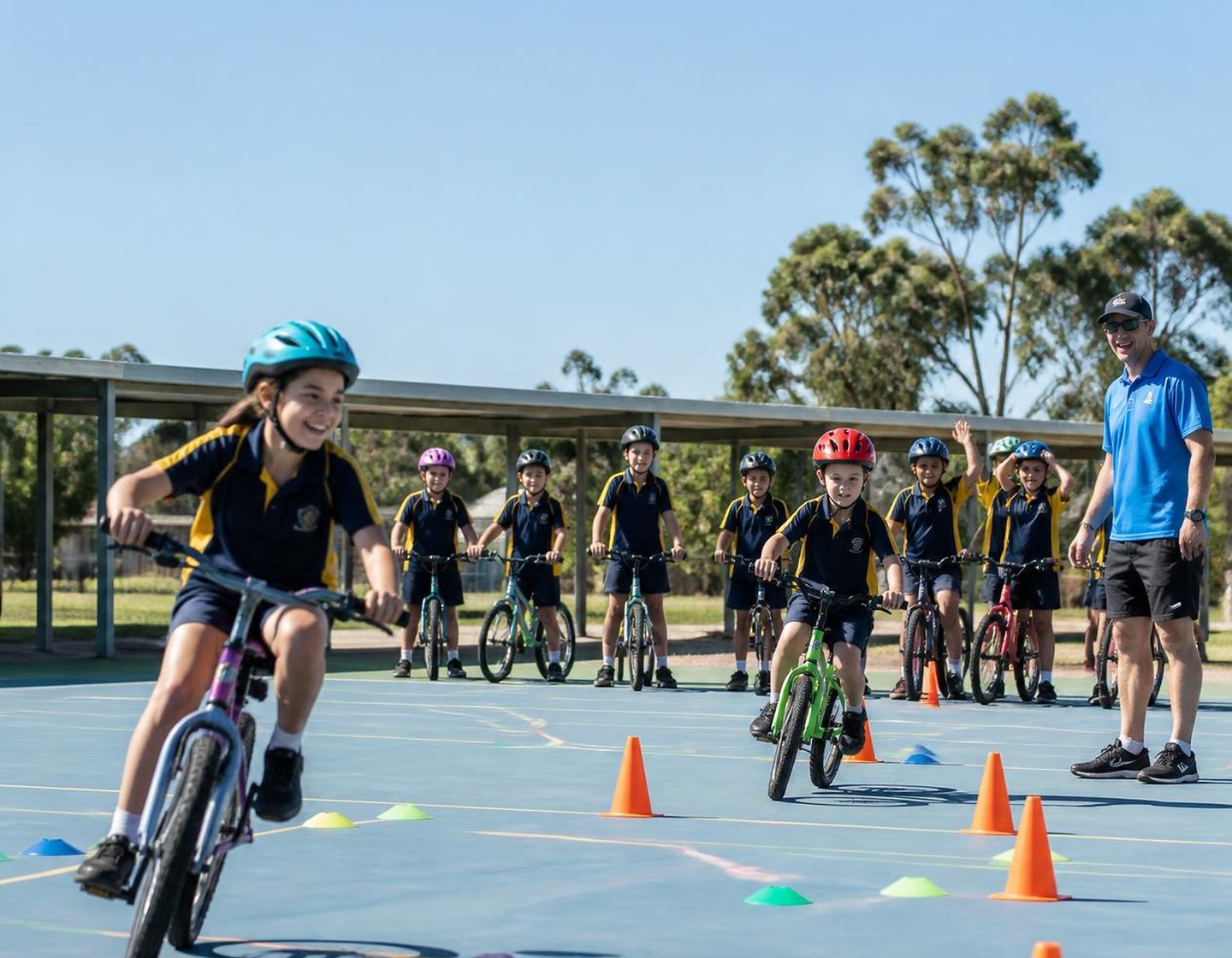 Primary school students on bikes riding a cone skills course on a school basketball court with a Bike On coach