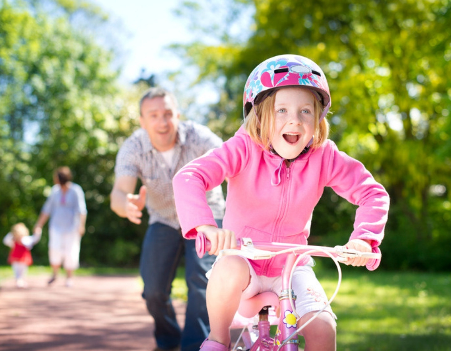 Dad letting go as his daughter rides off on her bike for the first time, smiling